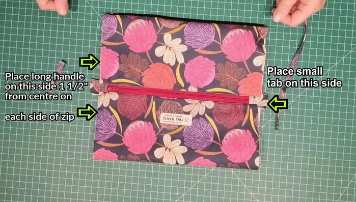 Attach handle and tab: Place handle pieces 1.5" from the center of each side, and attach tab to top of zipper on one side. Stitch in place.