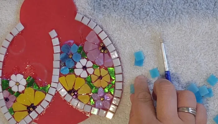 Glue the daisy-shaped tiles to form the ladybug's body. Continue filling in areas with the same techniques used for the wings.