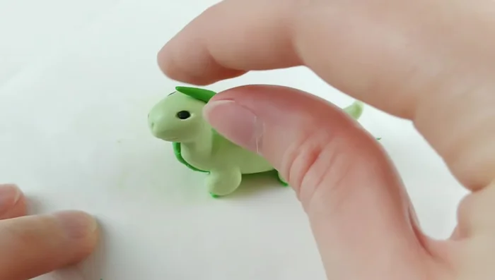 Roll a log of dark green clay, same length as the dragon, and add it along the back for a side bang, creating individual scales with a flat edge tool.