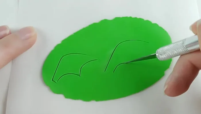 Roll out a thin sheet of dark green clay, cut into wing shapes. Add light green details for support and sections. Create a second wing by pressing the first onto parchment paper, flipping, and adding details to the second side.