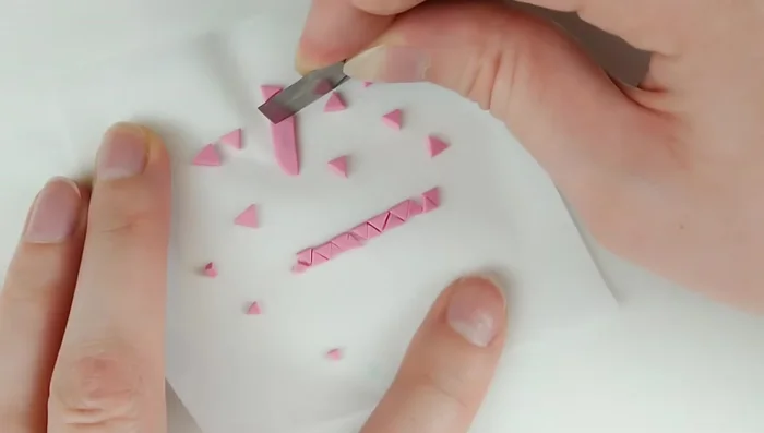 Cut out thin strips of dark pink clay, then cut them into various sized triangles. Bake for 5 minutes, cool, and separate. Attach triangles to the back, starting large and decreasing in size towards the tail, using liquid Sculpey and tweezers for placement.