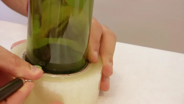 Use a glass cutter to score a line around the bottle, using tape to guide the cutter for a consistent score.