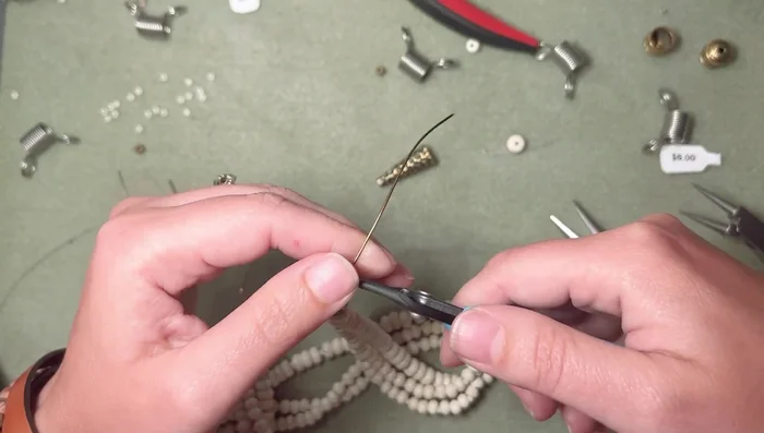 Create a loop at the top of the necklace using round-nose pliers. Secure with a small coil and cut off excess wire. Consider adding a small bead at the top of the loop to prevent wire from being sucked into the hole.