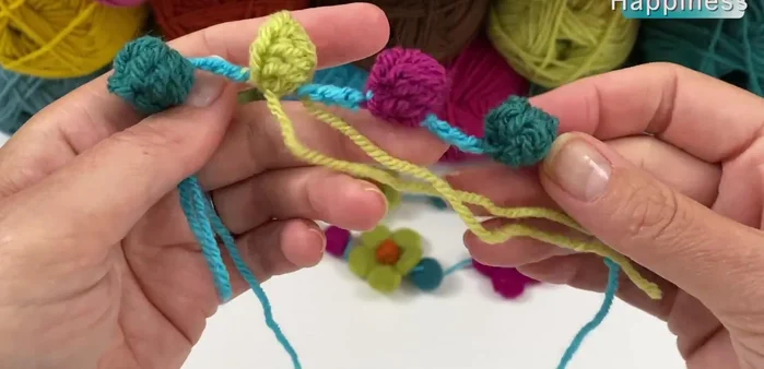 Repeat steps 2-4, using berry, pistachio, and teal yarn for subsequent popcorns, creating a sequence of four popcorn beads.