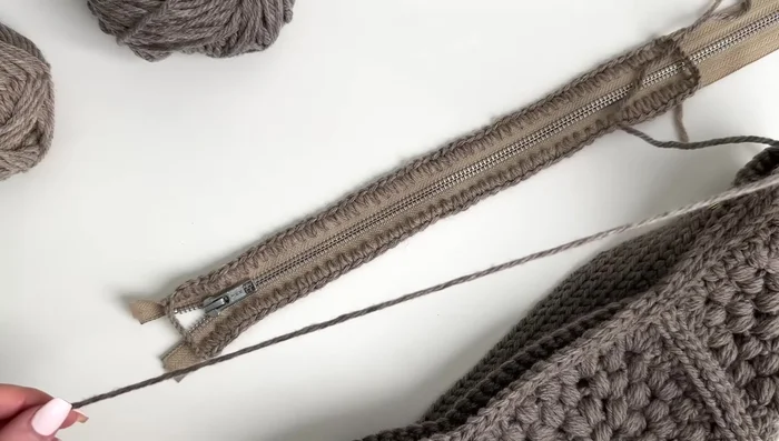 Sew along the edge of the bag, catching both the crocheted zipper and the bag's stitches. Ensure even stitching.