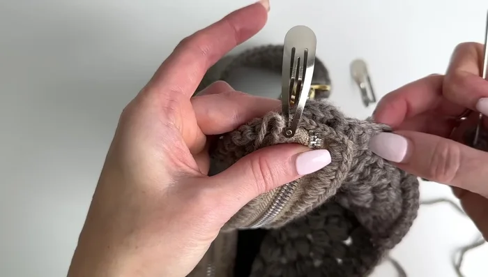 Sew along the edge of the bag, catching both the crocheted zipper and the bag's stitches. Ensure even stitching.