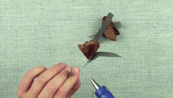 Prepare paper strips, hot glue the edge to the base of the flower, and wrap around the wire, twisting the stem. Glue the strip and cut off the excess.