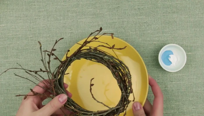 Prepare a twig wreath base. Paint the buds on the twigs with a contrasting color (e.g., light blue acrylic paint) to add volume.