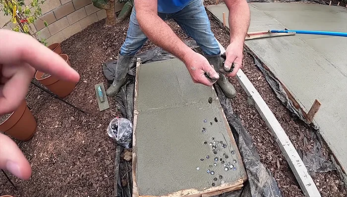 Spread glass beads over the wet concrete. Allow some beads to sink, reserving some for a later, less wet layer. Consider a pattern for better visual appeal (lazy river pattern used in video)
