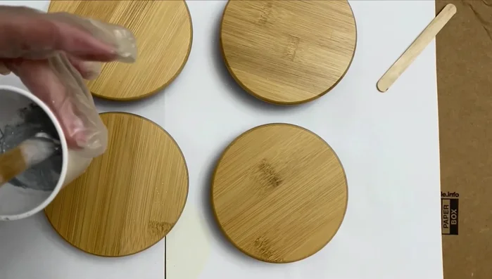 Apply epoxy to lids: Carefully drizzle the epoxy mixture onto the prepared bamboo lids, spreading it evenly to create a marble effect. A cardboard and paper underneath is recommended to prevent sticking.