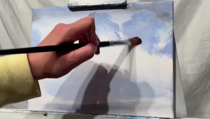 Switch to a smaller filbert brush. Use white paint to soften and blend the edges of the clouds, creating a gradual transition to the canvas.