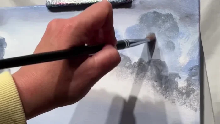 Saturate certain cloud areas with heavier paint to add depth and contrast, ensuring the clouds aren’t completely flat. Use a hint of white and blue to prevent clouds from looking completely black.