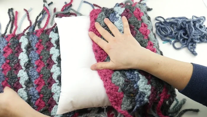 Seam the sides: Fold the rectangle in half with the right sides facing inwards. Using a tapestry needle and scrap yarn, seam the sides together using a whip stitch, leaving an opening at the top for inserting the pillow.