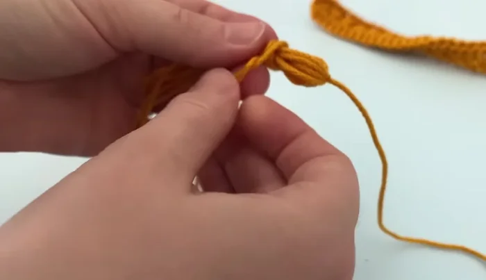 Shape the tassel: Wrap a new piece of yarn around the tassel 3-4 times and secure with a double knot. Trim the tail.