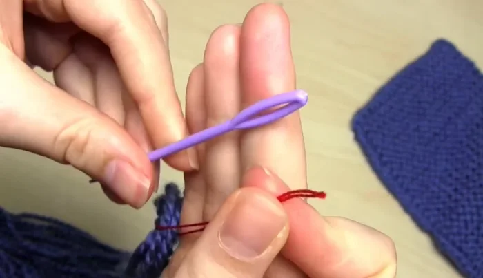 Remove the needle and thread. Put your fingers through the loop, grab the yarn ends, and pull them through to tighten.