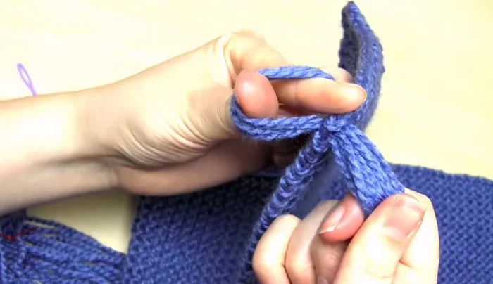 Remove the needle and thread. Put your fingers through the loop, grab the yarn ends, and pull them through to tighten.