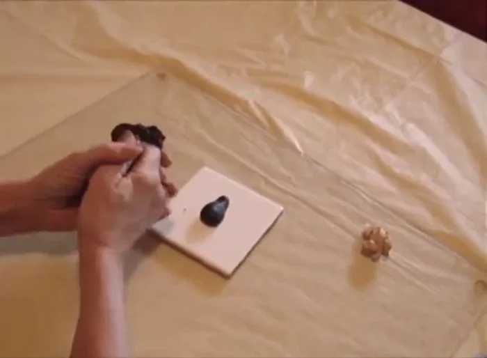 Create two front paws using small balls of black clay, roll them into cylinders, and attach them to the body. Use the needle to create claw marks.