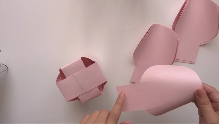 Layer the petals: Build the flower layer by layer, using the 'plus' formation for the first two layers and the 'X' formation for the subsequent layers, always ensuring a slight gap between petals and layers to create dimension.