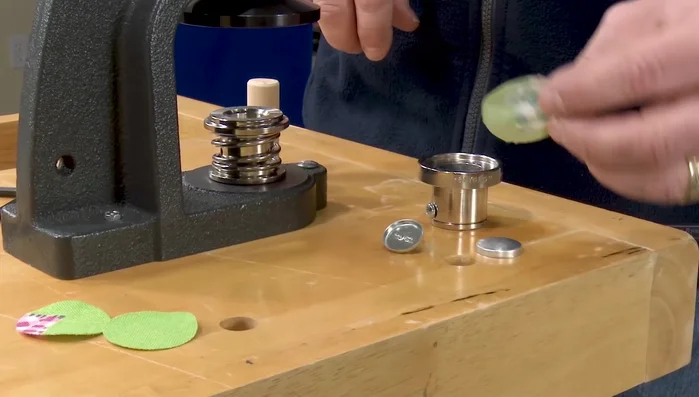 Use a dowel to press the button top and fabric into the concave portion of the die. Lift the outer collar.
