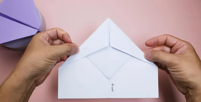 Fold the top of the airplane down to the marked position, then unfold. Fold the front part along the crease, extending it with a pen if needed, and fold downwards. Secure both wings inward.