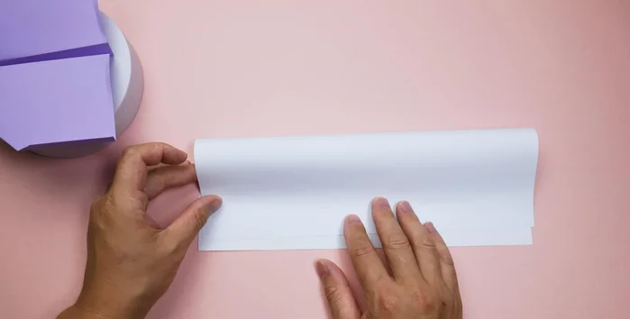 Fold the paper in half lengthwise, ensuring even folds on both sides. Press down the crease firmly.