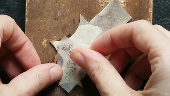 Draw designs and glue them onto a silver sheet using spray glue.