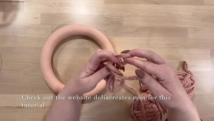 Create the initial slip stitch. Loop the yarn around the wreath, then pull a loop through with your fingers to form a slip knot.