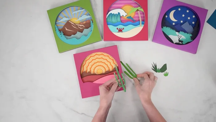 Add final details (e.g., cactus plants) using glue. Consider using Cubbies for support with complex layering.