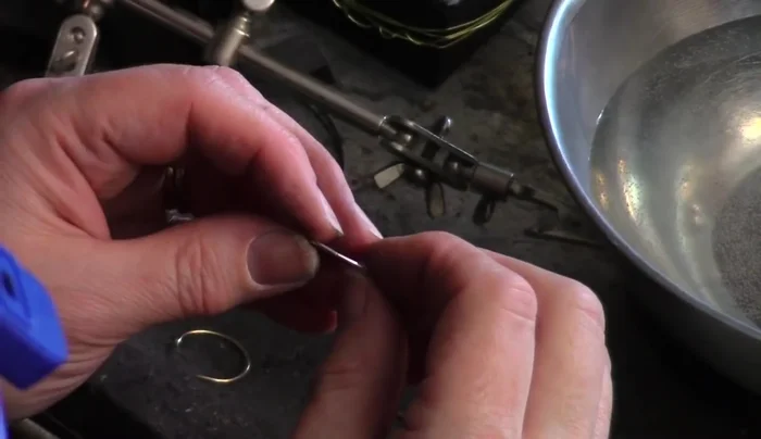 Solder the joint: Gently heat the ring with your torch before applying a tiny amount of easy solder paste. Heat the entire ring evenly in a circular motion to melt the solder and create a smooth, invisible joint. Quench the ring in water immediately after soldering.
