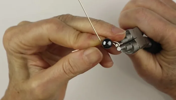 Use bail making pliers to create a loop at one end of the wire, centering it on one side of the bead. Repeat on the other side.