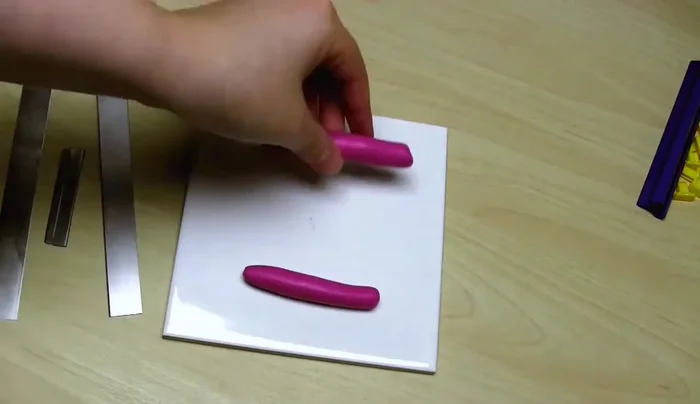 Create the two end pieces. Condition the remaining clay, make two sausage shapes. Cut a straight edge, fold it back on itself, press down except on the fold. Add a small clay sausage to the straight edge. After baking the main section, use it as a guide to cut the end pieces to the same width. Add ribbon effect, bake.