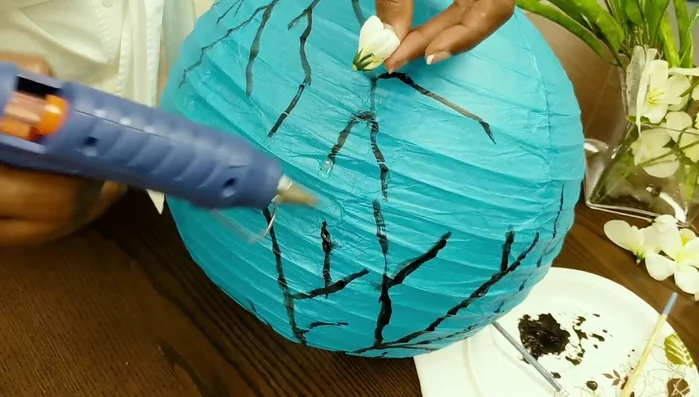 Attach flowers to the lantern: Apply hot glue to the lantern's branches and attach the flowers, holding them open as needed until the glue sets.