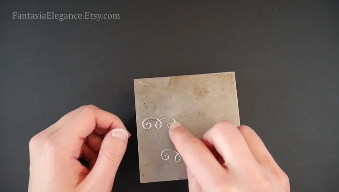 Hammer the overlays: Gently hammer the swirls of the overlay pieces using a jeweler's hammer and steel bench block to flatten them slightly, reshaping after hammering each piece to maintain symmetry.