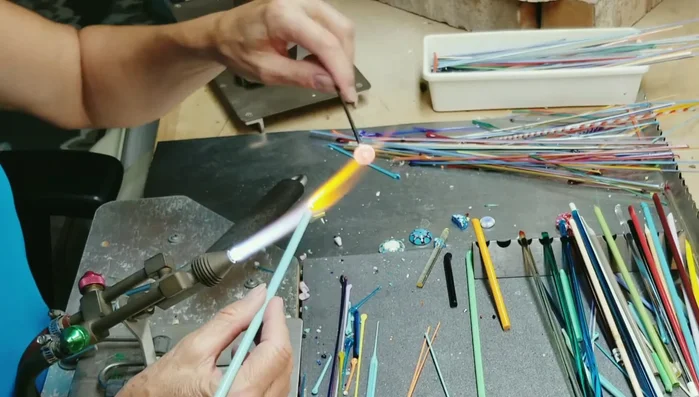 Using a graphite paddle, spread the turquoise glass to the outside edge of the mandrel, ensuring it's evenly distributed.