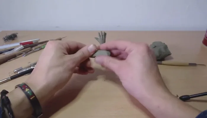 Create a basic hand shape: Start with a clay blob and roll it into a thick snake shape. Then, pinch and shape it into a rough, slightly curved form resembling a hand.