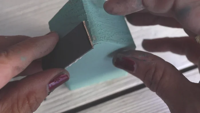 Attach popsicle sticks to the house: Apply wood glue to the back of the unpainted popsicle sticks and glue three pieces to each side of the house.