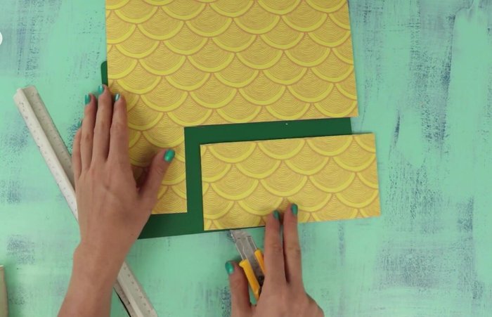 Cut and glue colored poster board pieces onto the wood to create decorative elements.