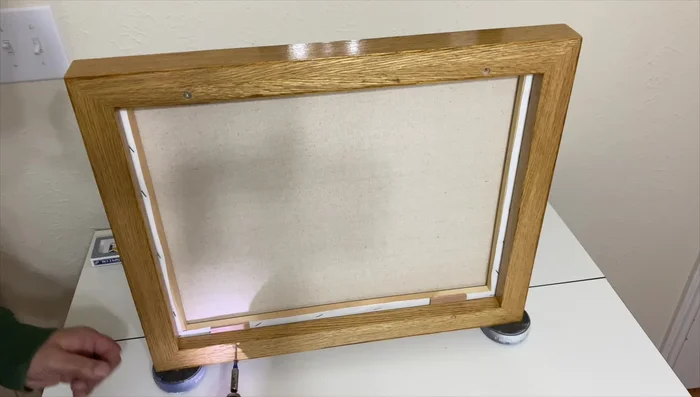 Attach the painting to the frame using the mounting plates and screws.