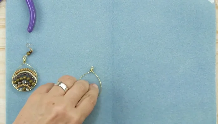 Add the first row of beads: Wrap one end of the 28-gauge wire around the hoop base several times. Add the first row of beads, ensuring they are centered below the loop.