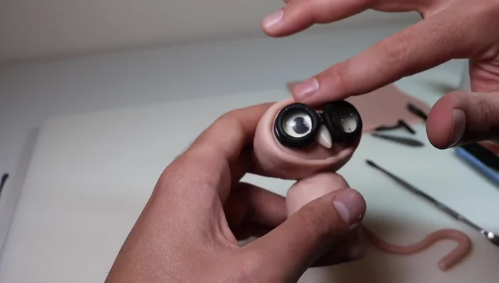 Create and attach the hood using a snake of clay, blending it into the head. Add feathers to the forehead and texture the hood.