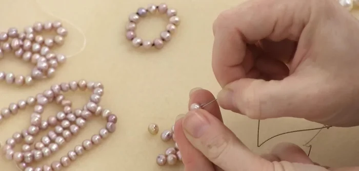 String on the first bead: Thread the needle through the chosen bead and pass it through a second time to ensure you can pass through twice. Slide it down to the tape.