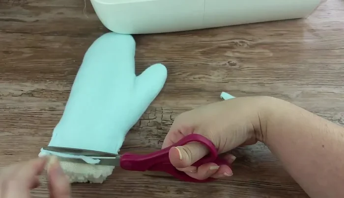 Trim ¼ inch off the top fabric. Fold the inner fabric ends in by ¼ inch, then fold it over by ¼ inch on the long side. Fold it up over the top fabric by about ½ inch and stitch across, using a backstitch. Sew only one side of the wrist, leaving the opening for your hand.