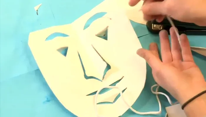 Position the string on the back of the mask near the top of the eyes and staple it in place. Repeat on the other side. Cover staples with masking tape for comfort.